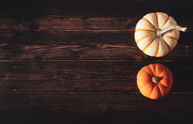 two miniature pumpkins sitting side by side on a wooden surface