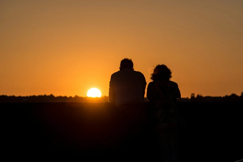 a man and woman watching the sun set in the distance