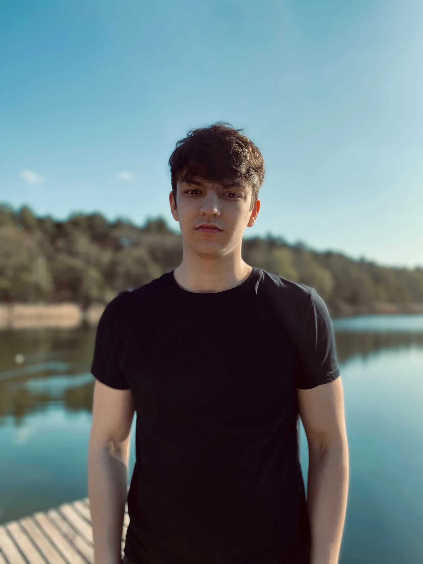 a man in black shirt standing on pier next to water