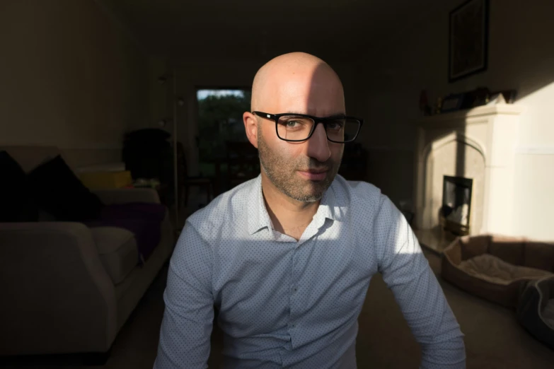 a man with bald hair and glasses standing in front of a couch