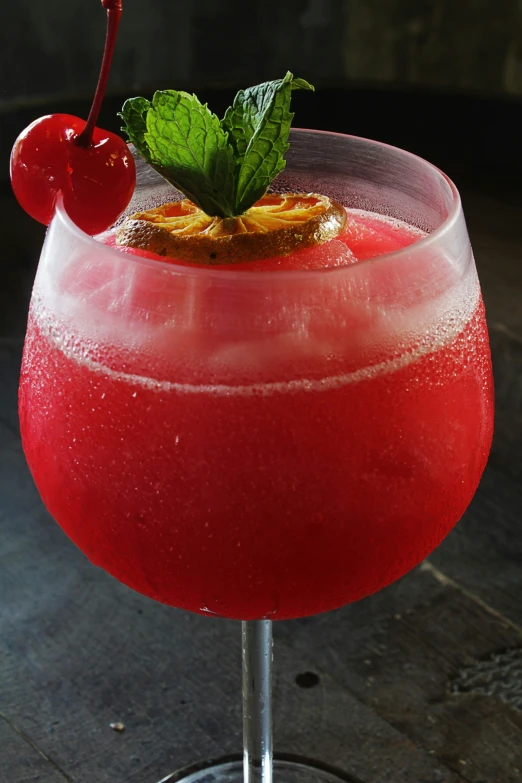 a red beverage with garnish and mint in a glass