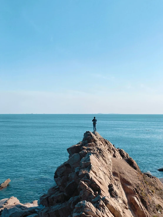 a person stands on a small rock ledge looking at the ocean