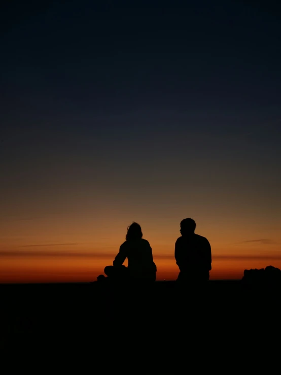 two people sitting on a hill as the sun sets