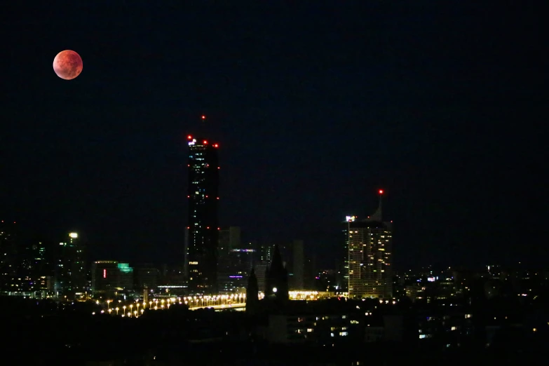 city skylines in the night with a large red ball in the sky