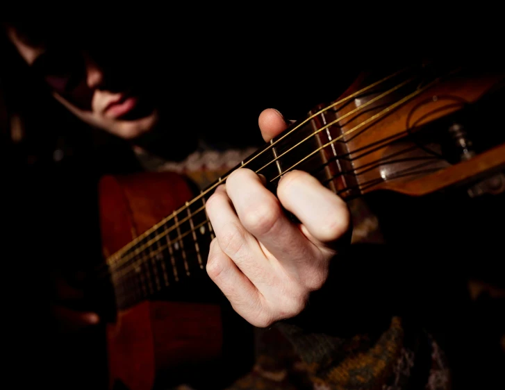 person's hand playing guitar on dark background