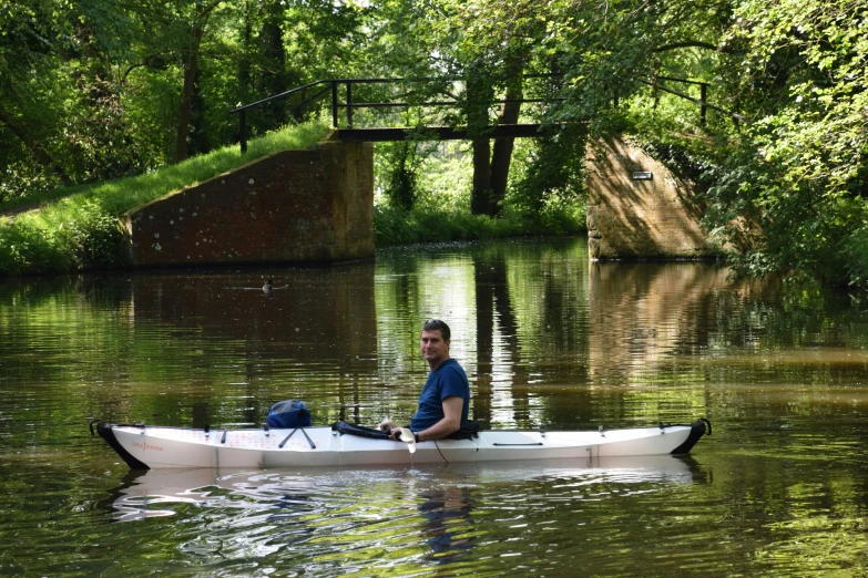 the man is canoeing on the river near an old bridge