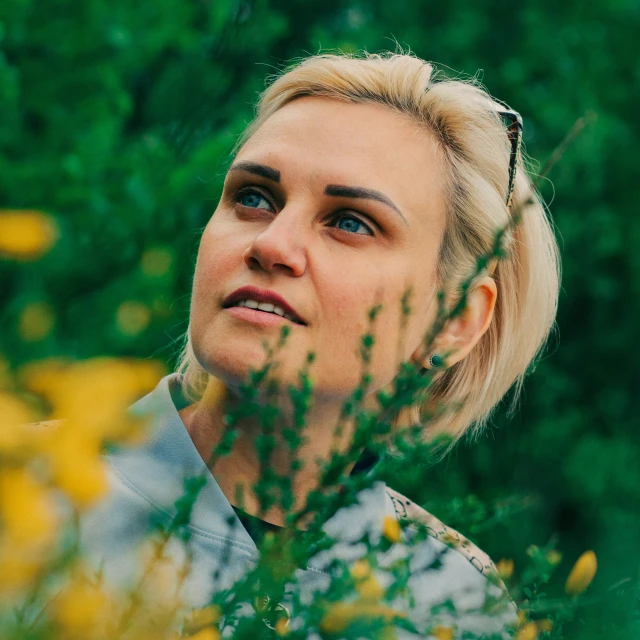 a blonde female looks into the distance while surrounded by wildflowers