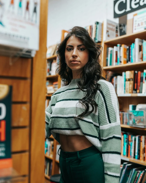 a young woman stands in front of a book shelf and looks to the side