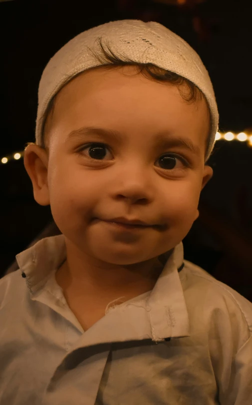 an adorable young child is wearing a white cloth over his head