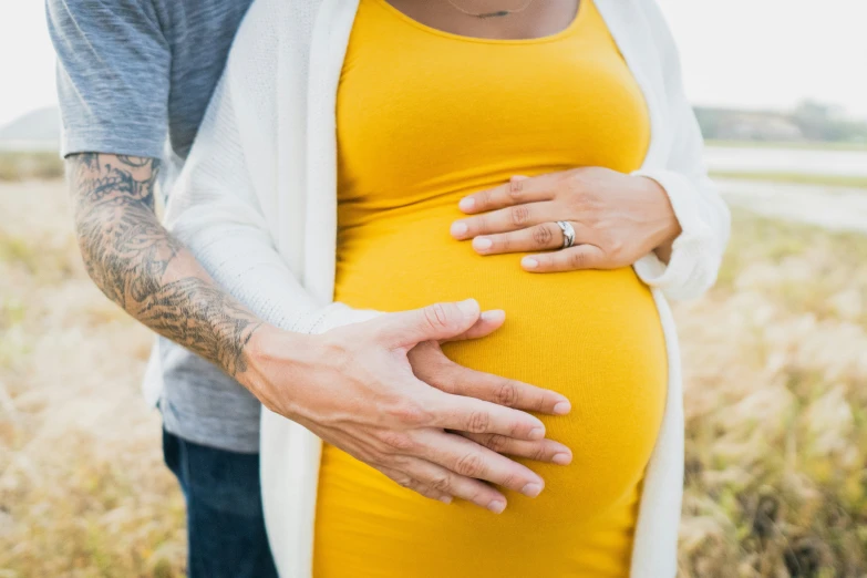 a pregnant woman's hand on her stomach and the belly of a man who is holding a baby bump