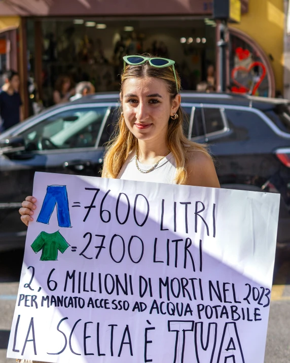 a girl holding a sign in front of some parked cars