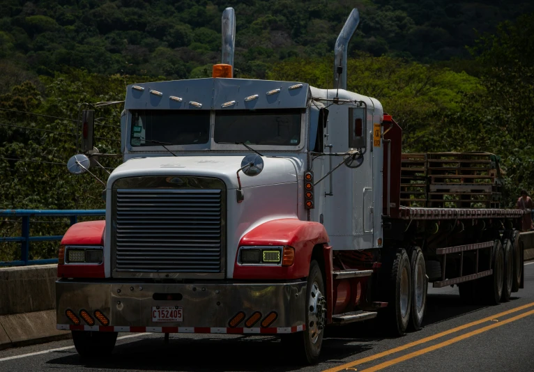 a semi truck traveling on the road with trees in the background