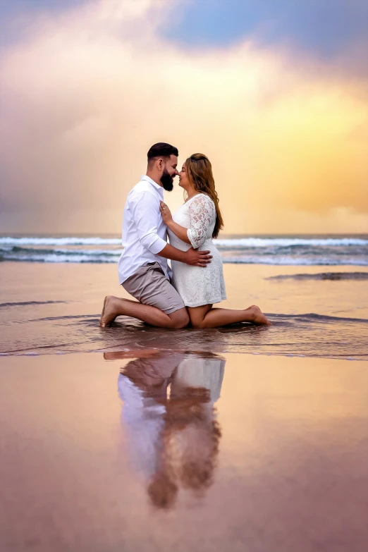 an engaged couple is sitting in the shallow water on the beach