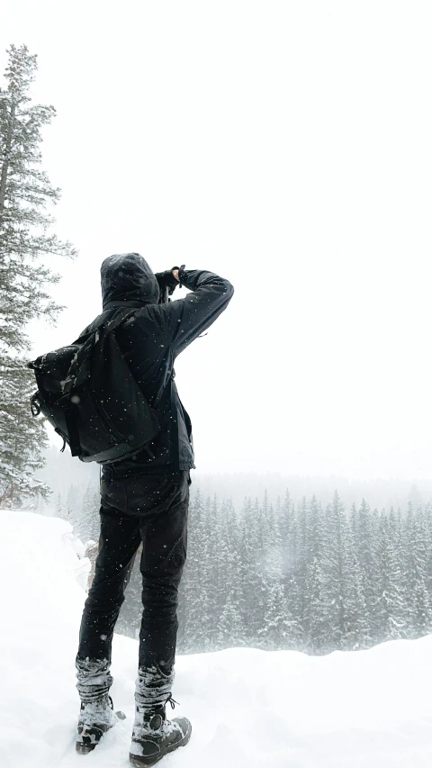 a person standing on a snow covered hill looking through binoculars