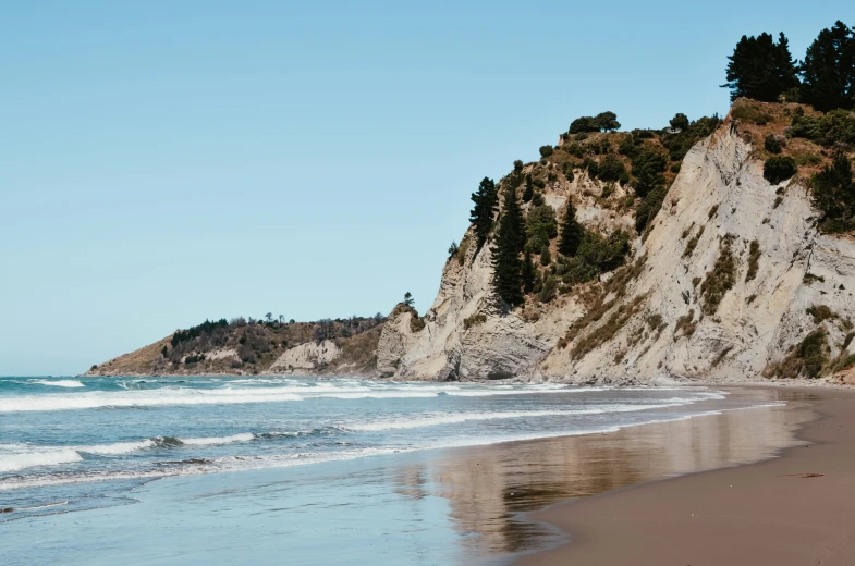 a beach scene with a cliff and wave coming ashore