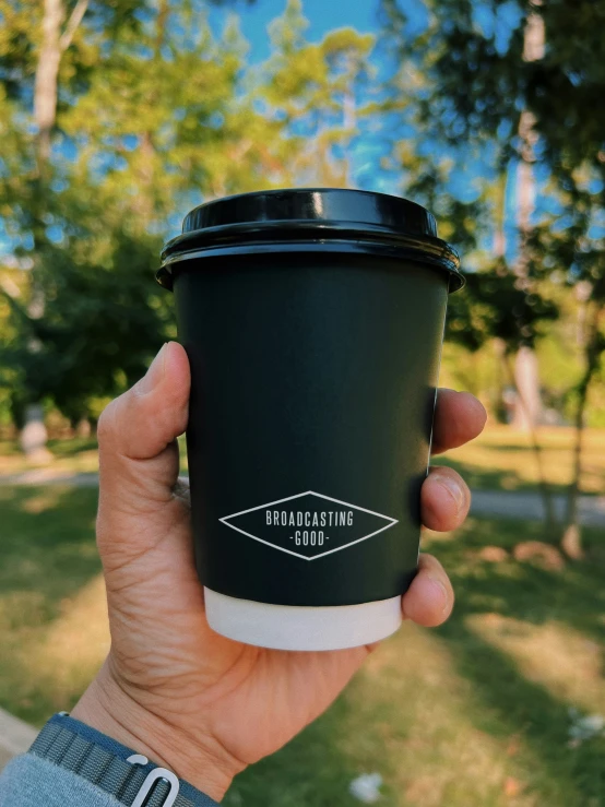 someone holds a cup with a black plastic cover