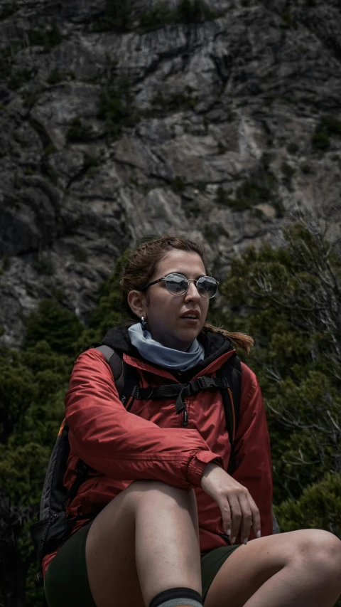 a woman is sitting on a cliff looking at the camera