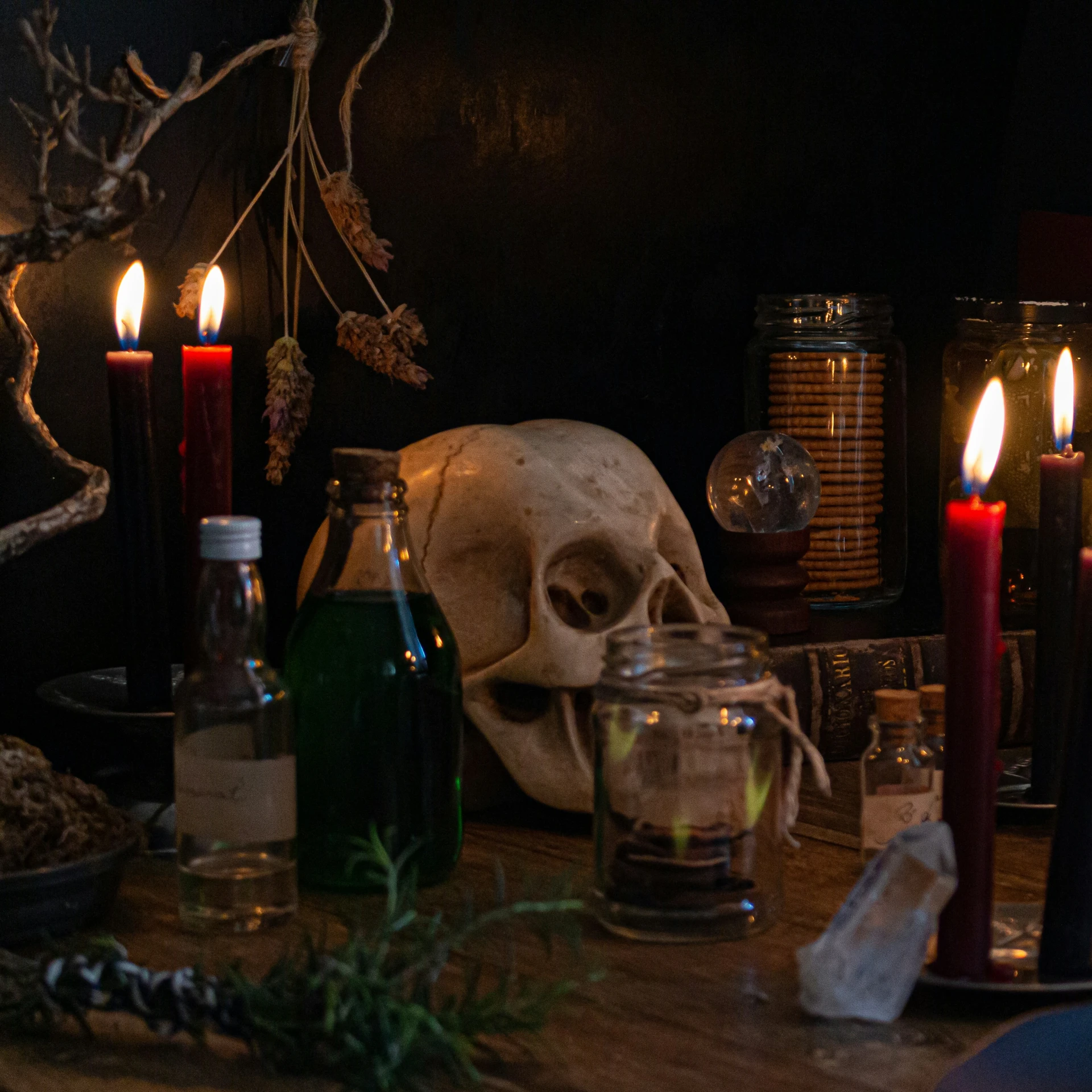 a lit candle with three red candles and a skull head on a table