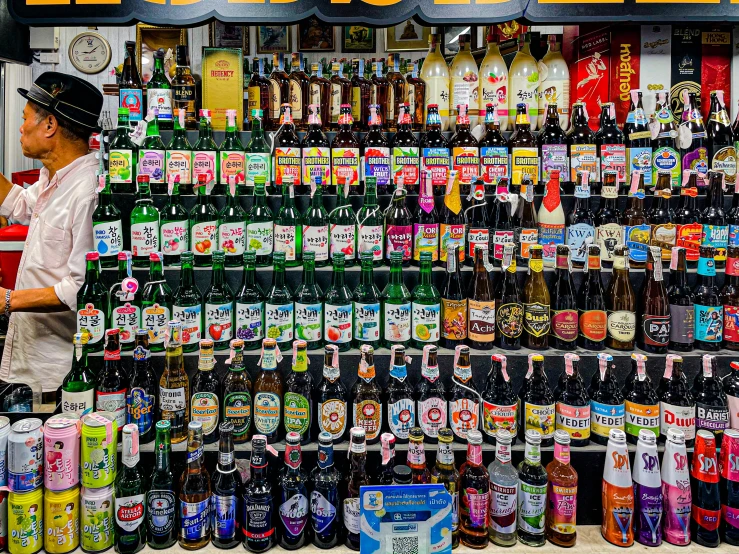 an asian man selling many kinds of alcohol bottles