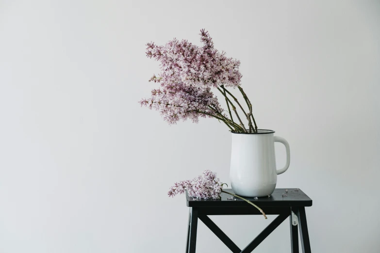 a white pitcher holding some flowers sitting on a small stand