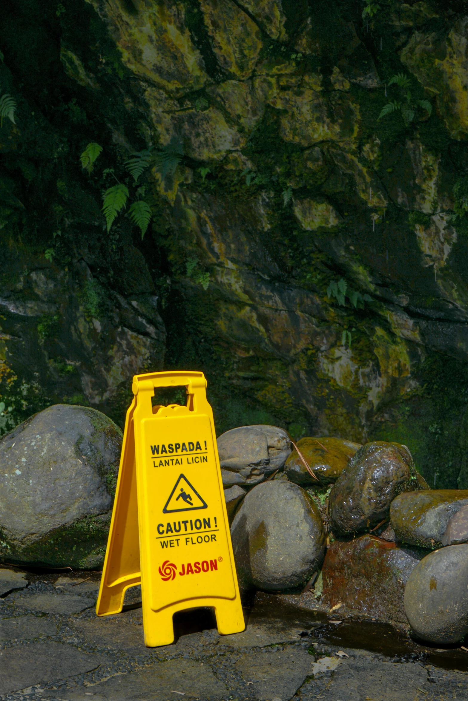 yellow sign sitting on the pavement beside rocks