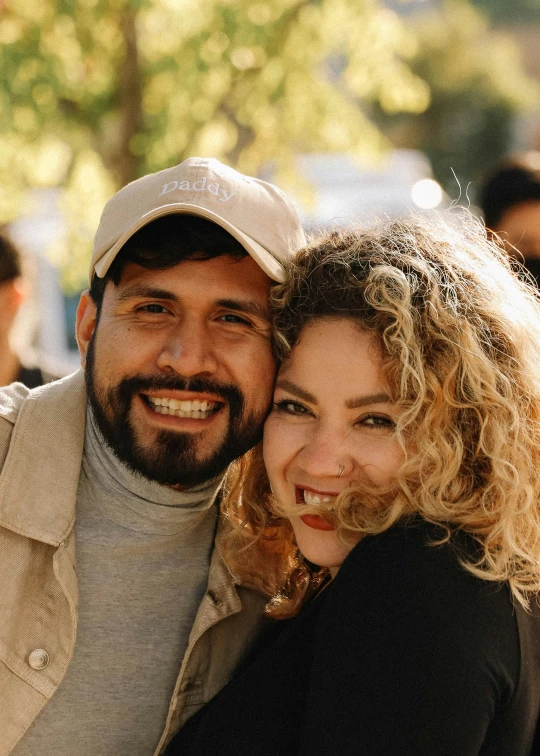 two people smile and hug with a tree behind them