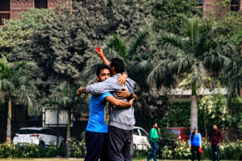 three men hugging and emcing each other while people play in the background