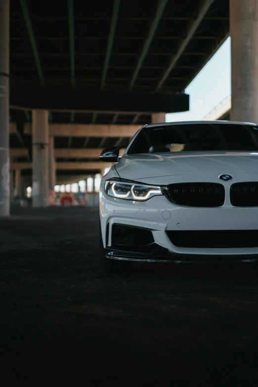 the front of a white bmw car, parked beneath an overpass