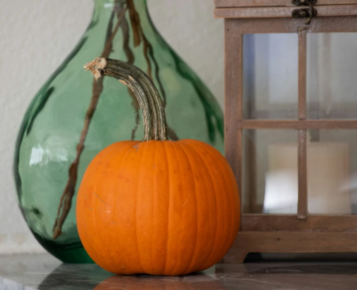 a pumpkin is sitting next to a glass vase