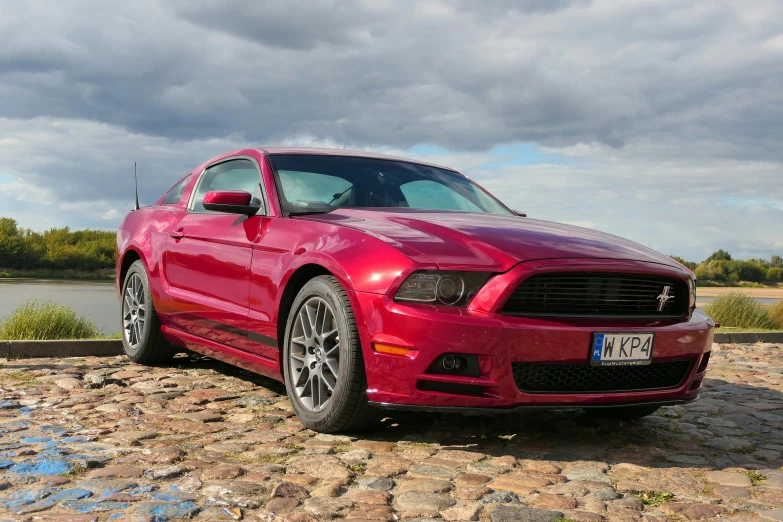 a red mustang parked in front of a lake