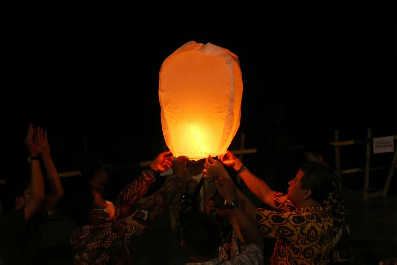 two men are holding up a lit paper lantern