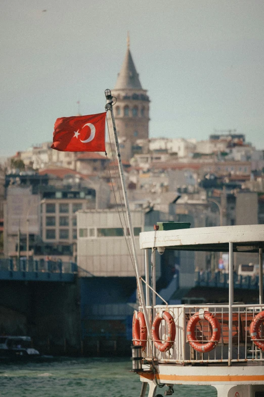 a ferry with a turkish flag on top and buildings in the background