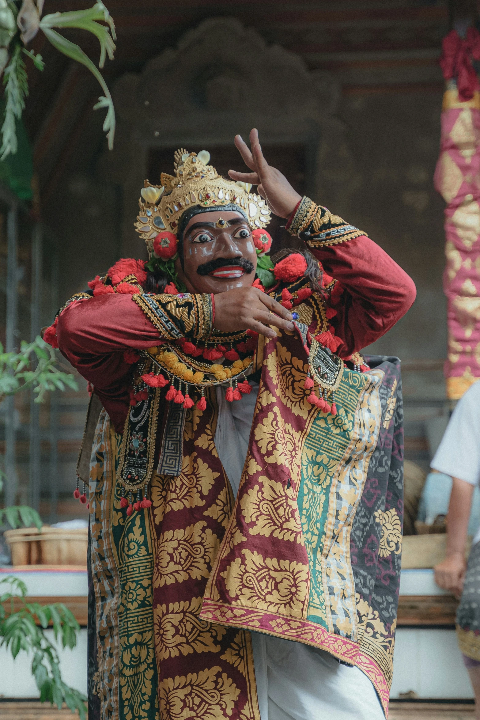 a smiling man wearing colorful clothing standing with hands to his head