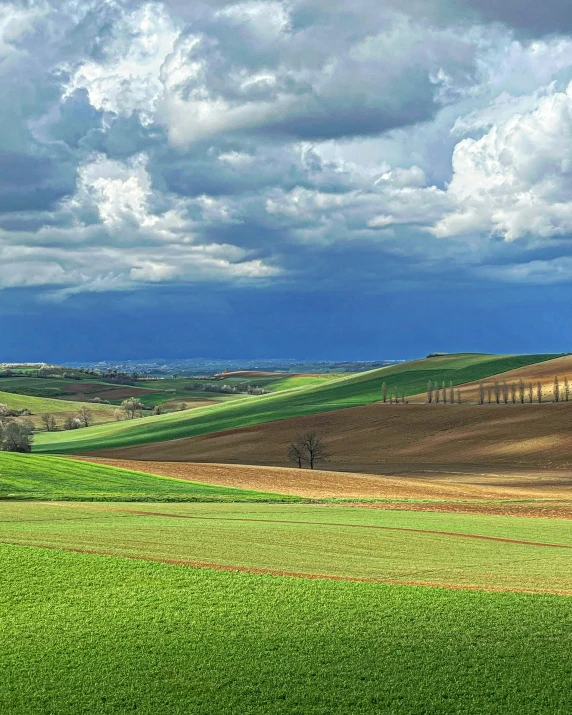 the clouds in the blue sky are over rolling fields