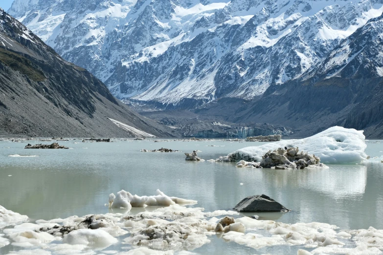 a large mountain range next to a lake and snowy mountains