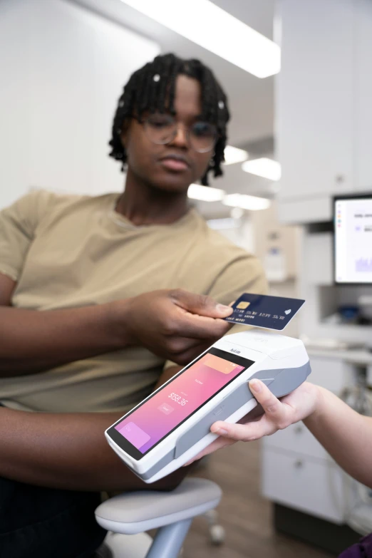 a boy holding up an iphone with one hand and another holding a credit card in the other