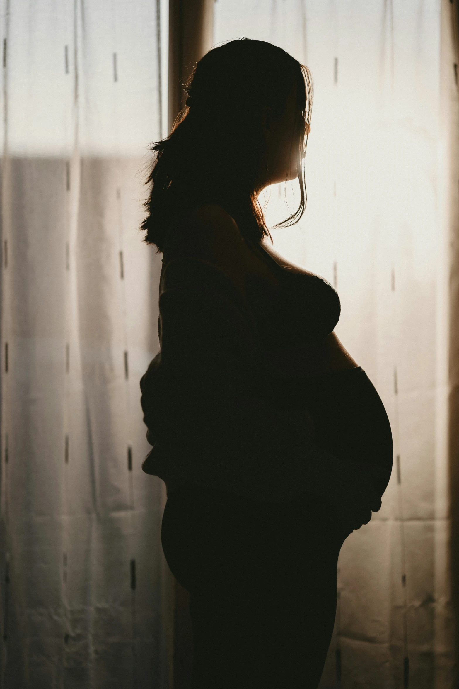 silhouette of a woman standing next to a curtain with her belly exposed